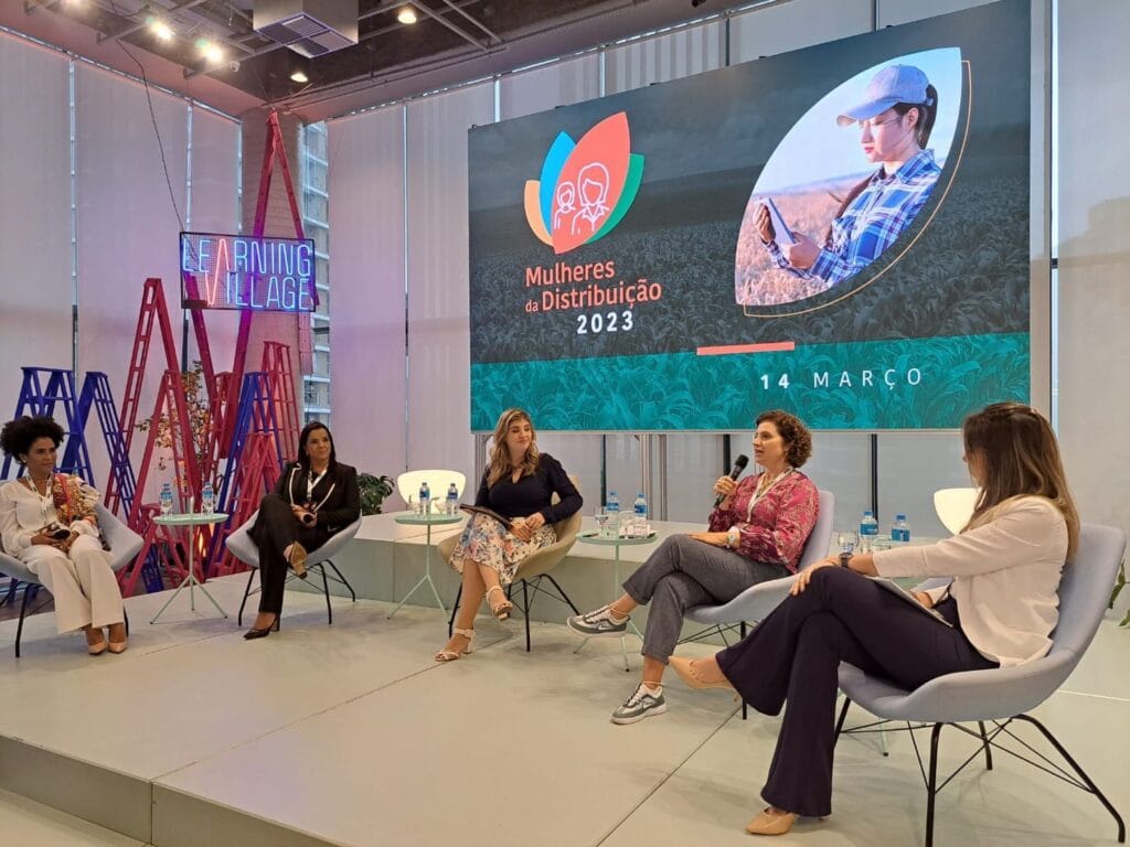 Painel Mulheres da Distribuição 2023: mulheres sentadas no palco, uma delas falando ao microfone